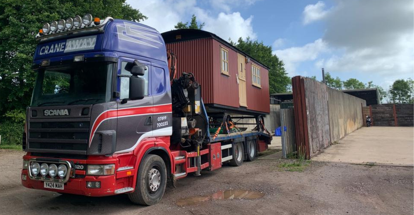 A red and blue Hiab transports a red shepherd hut
